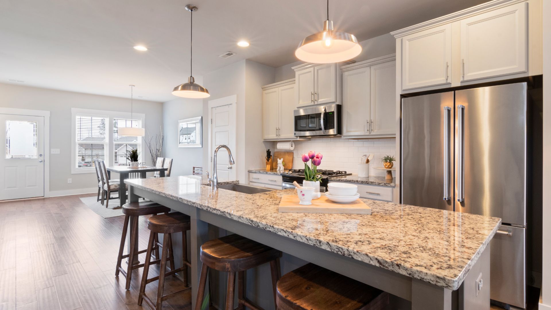 Modern kitchen with granite island, cream cabinets, stainless steel appliances, and pendant lights