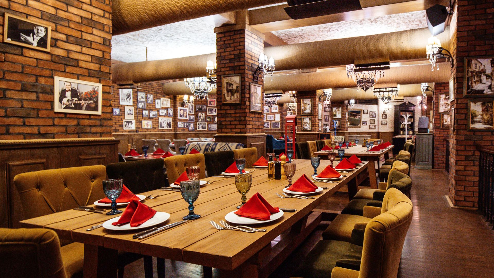 Upscale restaurant dining room with brick walls, vintage photos, long wooden tables, and red napkins.