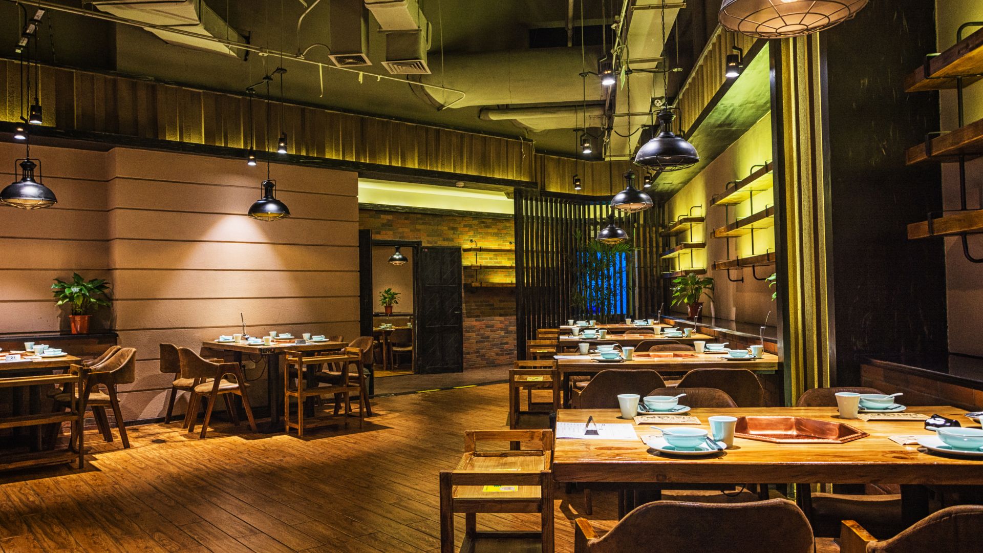 Modern restaurant interior with wooden tables, pendant lights, and warm yellow lighting ambiance.