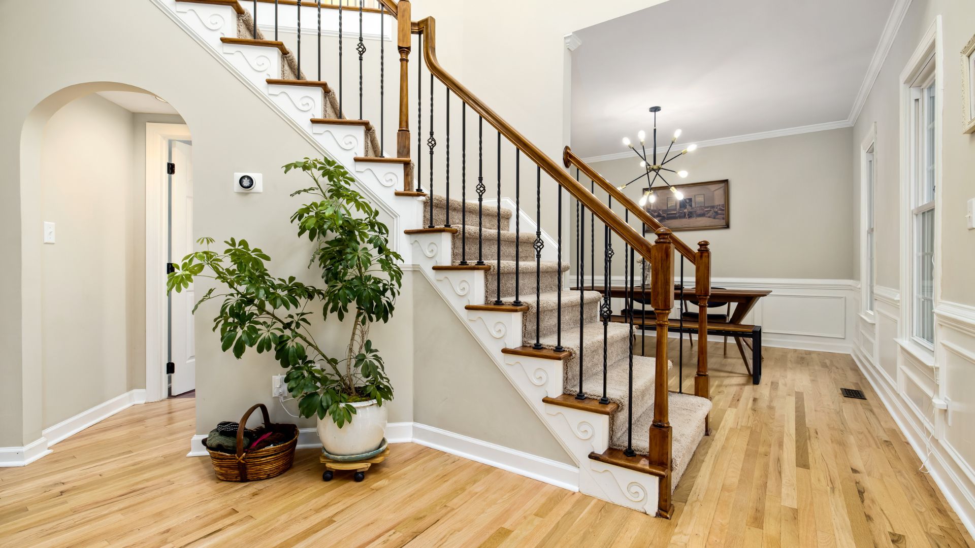 Elegant foyer with wooden staircase, metal railings, plant, and hardwood flooring throughout.