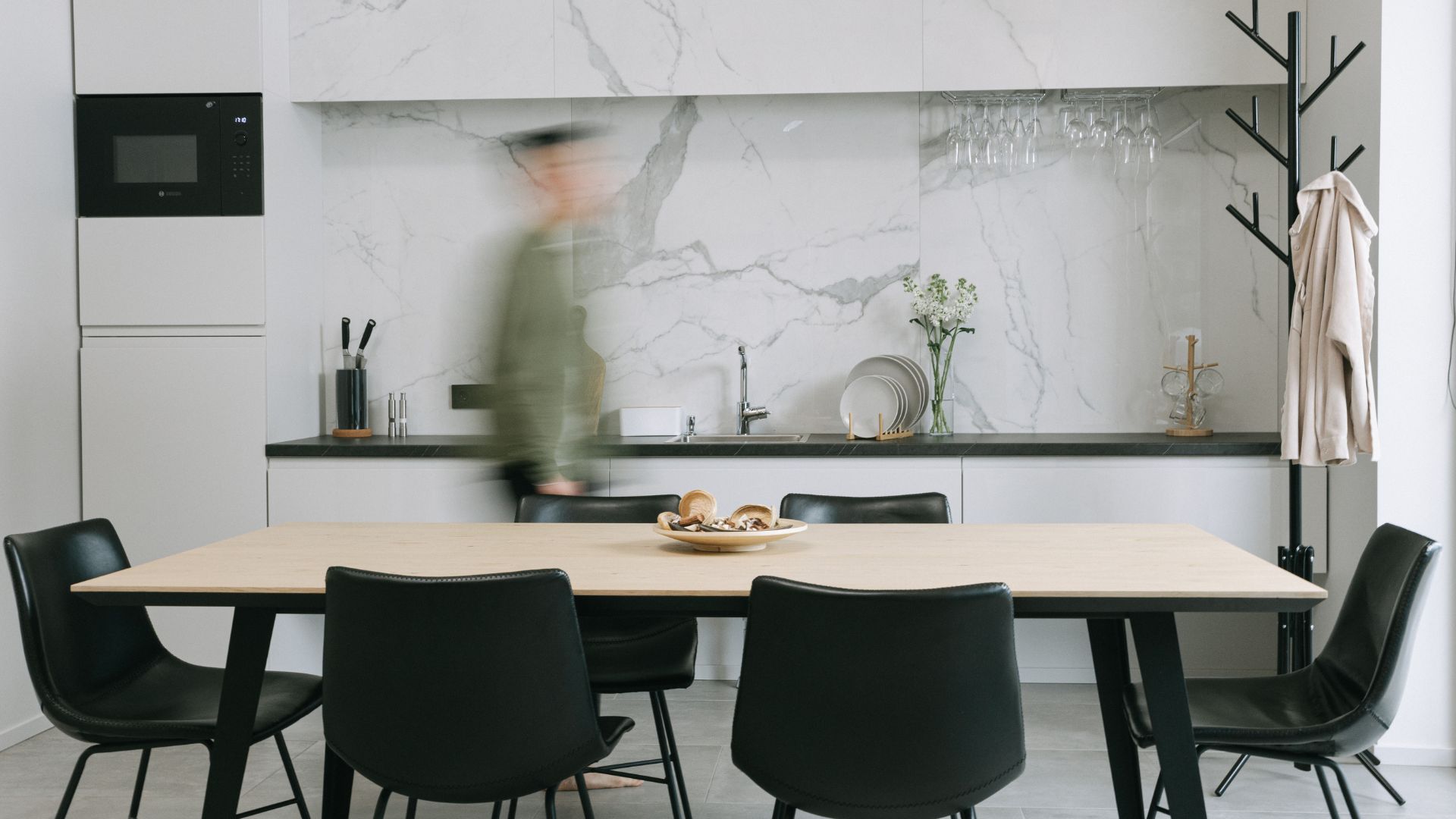Modern kitchen and dining room with marble backsplash, wooden table, and black chairs.